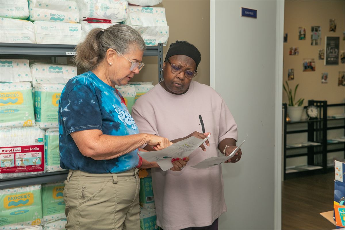 Two women reviewing paperwork in front of diaper shelves at the Oxford Diaper Bank